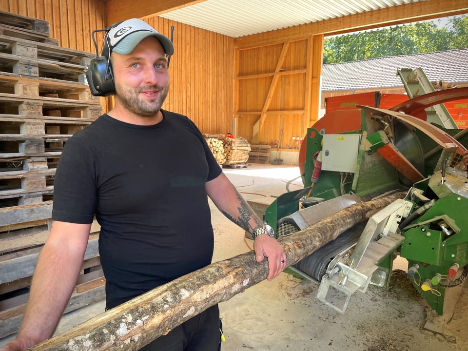 Luca Wüest hebt einen Baumstamm in die Holzspaltmaschine.