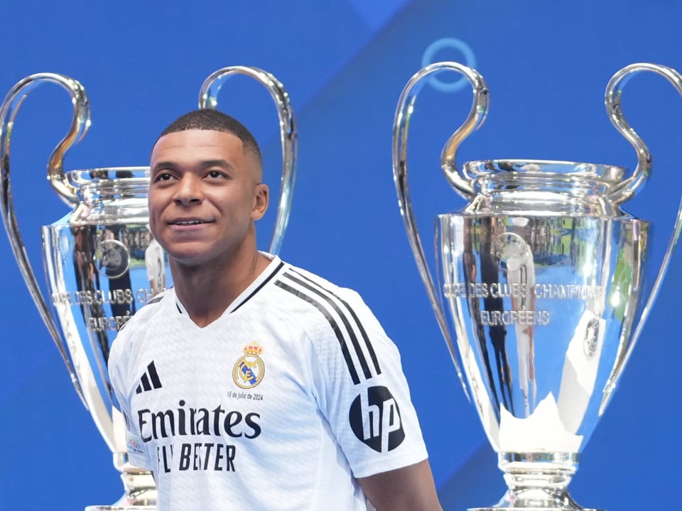 Soccer player next to two trophies on blue background.