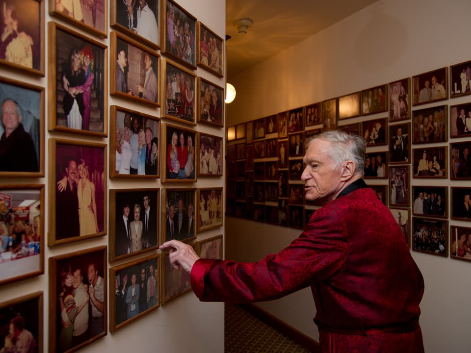 Der Playboy-Gründer Hugh Hefner im Bademantel vor einer Fotogalerie.
