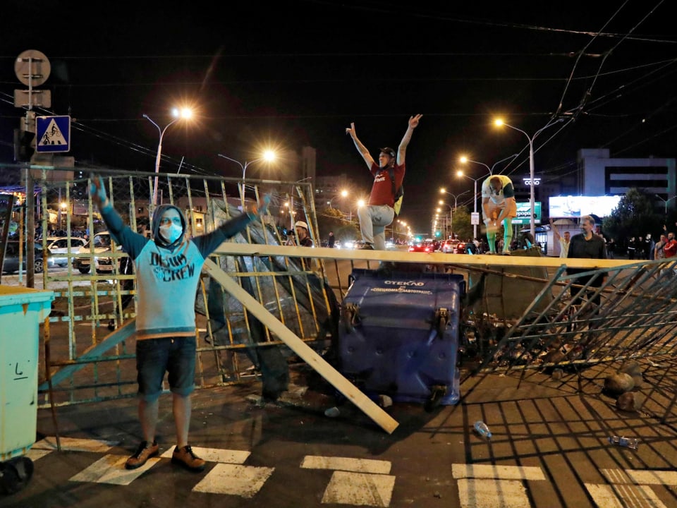 Protestierende haben eine Barrikade errichtet und blicken mit erhobenen Armen in die Kamera.