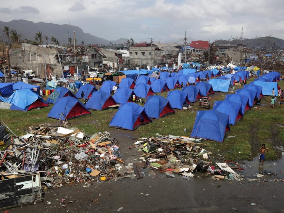 Viele Zelte neben einer verwüsteten Stadt.
