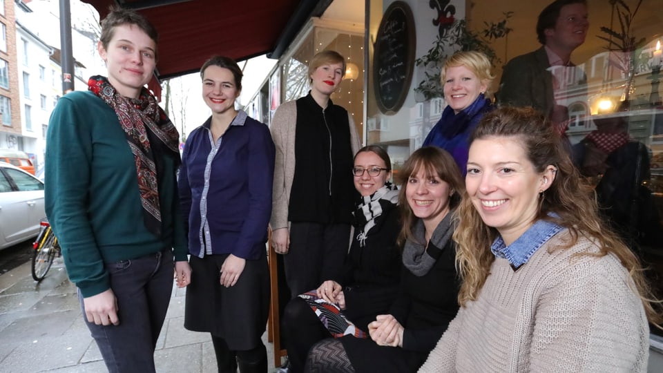 Sieben Frauen sitzen und stehen vor einem Café.