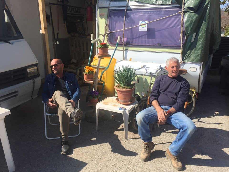 Zwei Männer sitzen vor einem Wohnwagen.