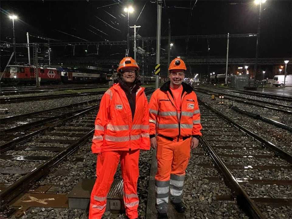 Reporterin mit Gleisarbeiter, beide in orangen Uniformen