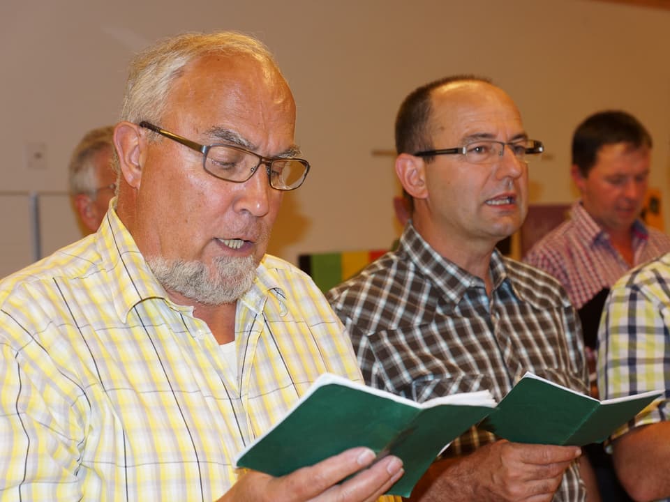 Eine Gruppe von älteren und jüngeren Sängern halten Notenbücher in der Hand und singen.