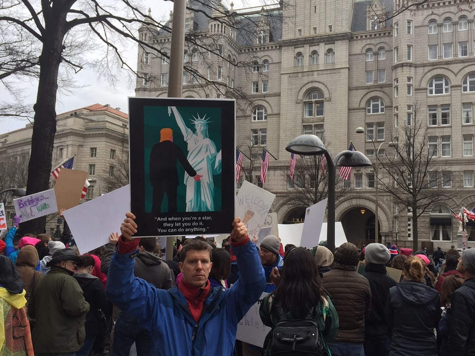 Demonstranten halten Plakate gegen Trump in die Höhe.