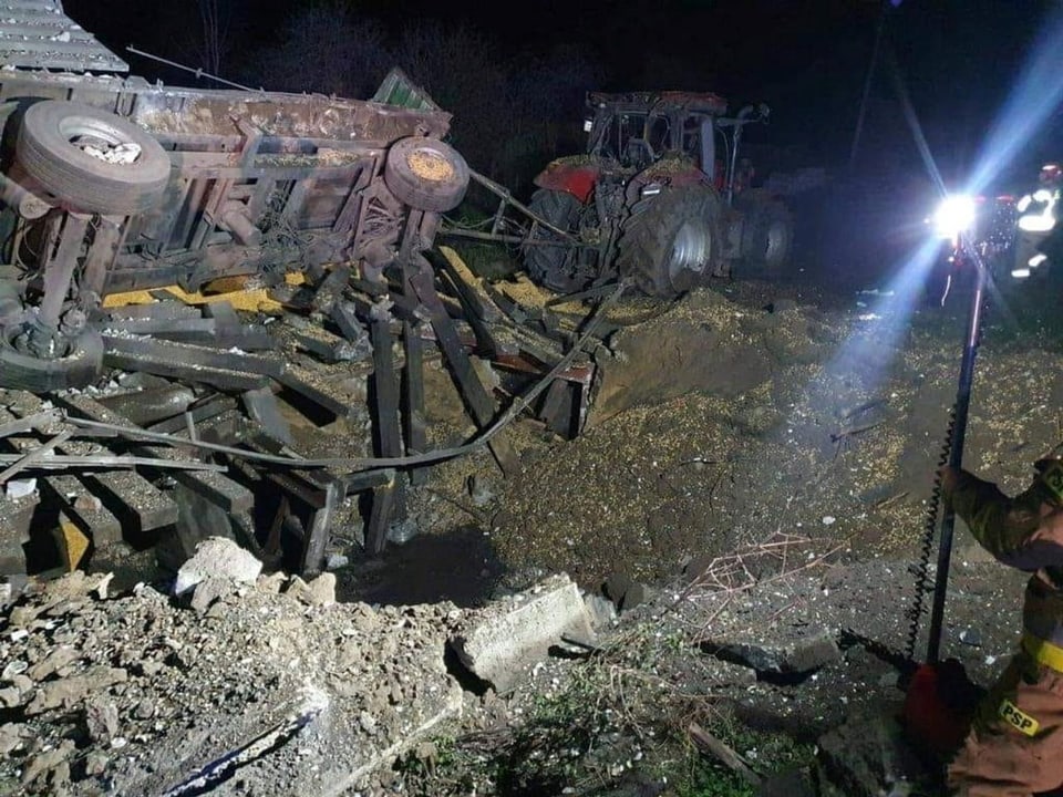 Bild eines tiefen Raketenkraters neben einem Traktor mit Anhänger. Das Fahrzeug ist zerstört.
