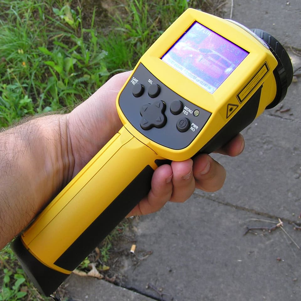 Eine Männerhand hält eine professionelle Wärmebildkamera mit gelbem Gehäuse.