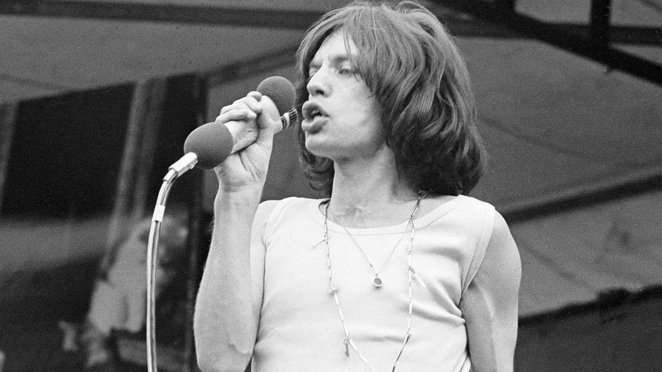 Schwarz-Weiss-Bild von Mick Jagger im Tank Top auf der Bühne. 