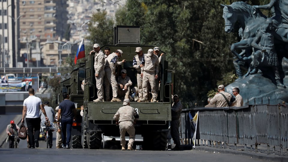 Russische Soldaten auf einem Militärlastwagen neben einem Denkmal.