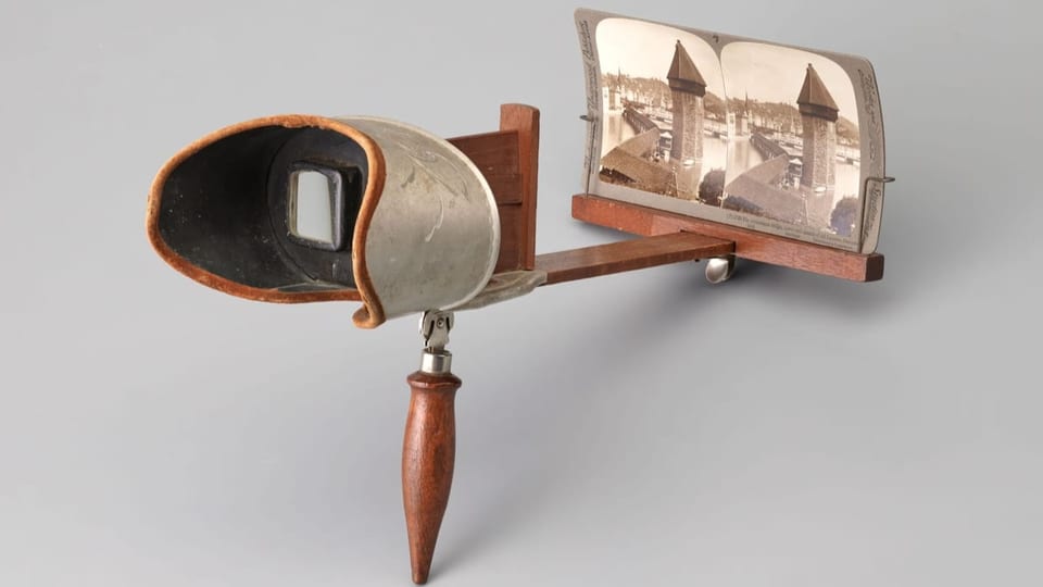 Ein altmodisches Gerät, mit einer Art Brille, durch die man auf eine eingespannte Fotografie blicken kann. 