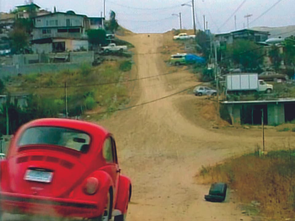 Ein Standbild aus einem Video zeigt einen roten Käfer, der über eine unbefestigte Strasse fährt.