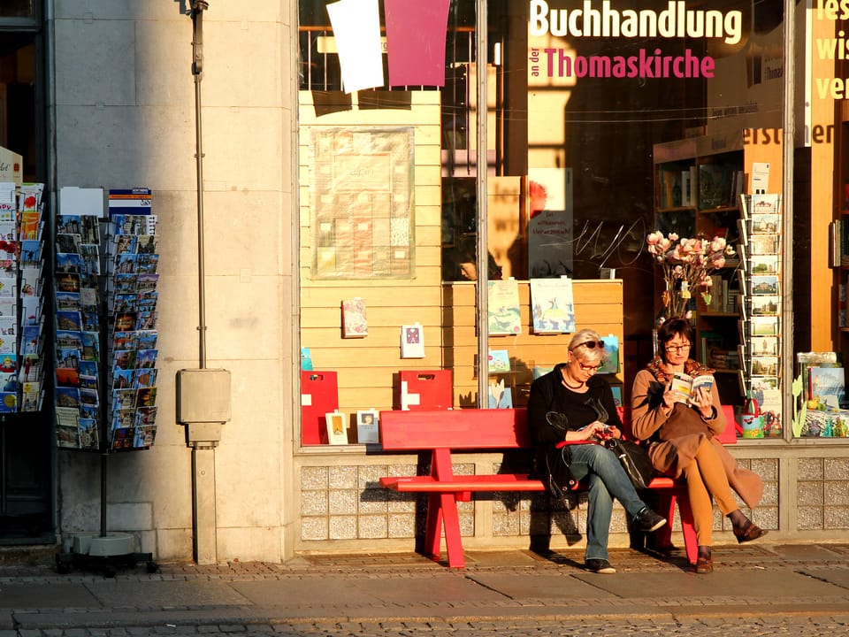 zwei Frauen sitzen auf einer roten Bank und lesen.