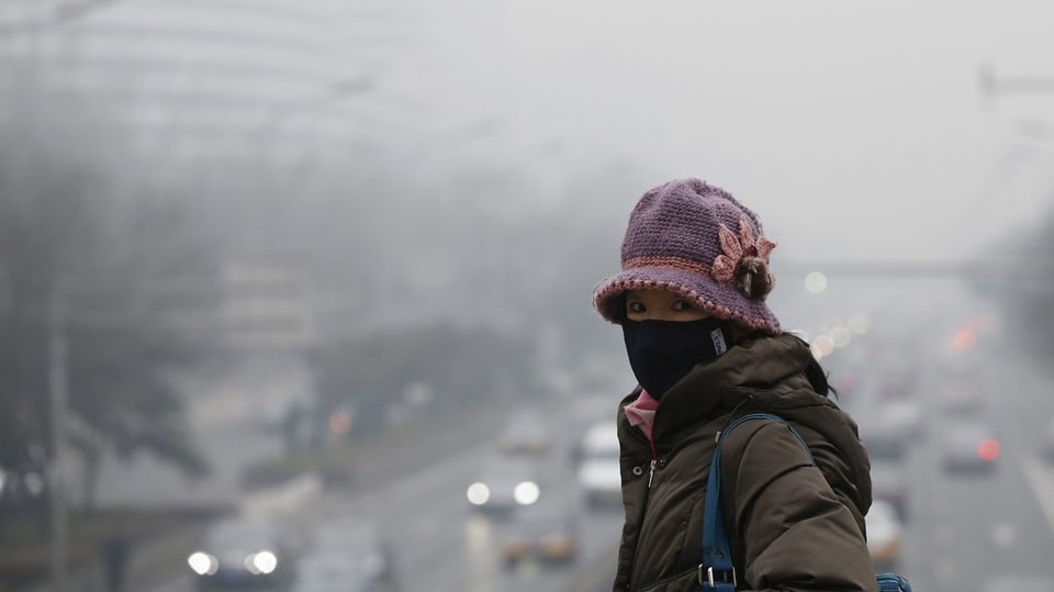Chinesische Frau mit Mundschutz vor Stadt mit Smog