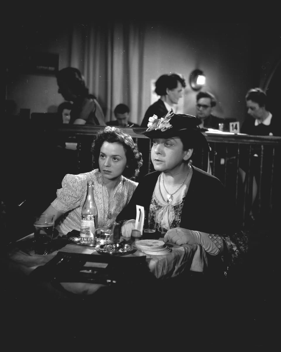 Eine Frau und ein Mann sitzen an einem Tisch in einem Restaurant und blicken in die andere Seite des Raumes.