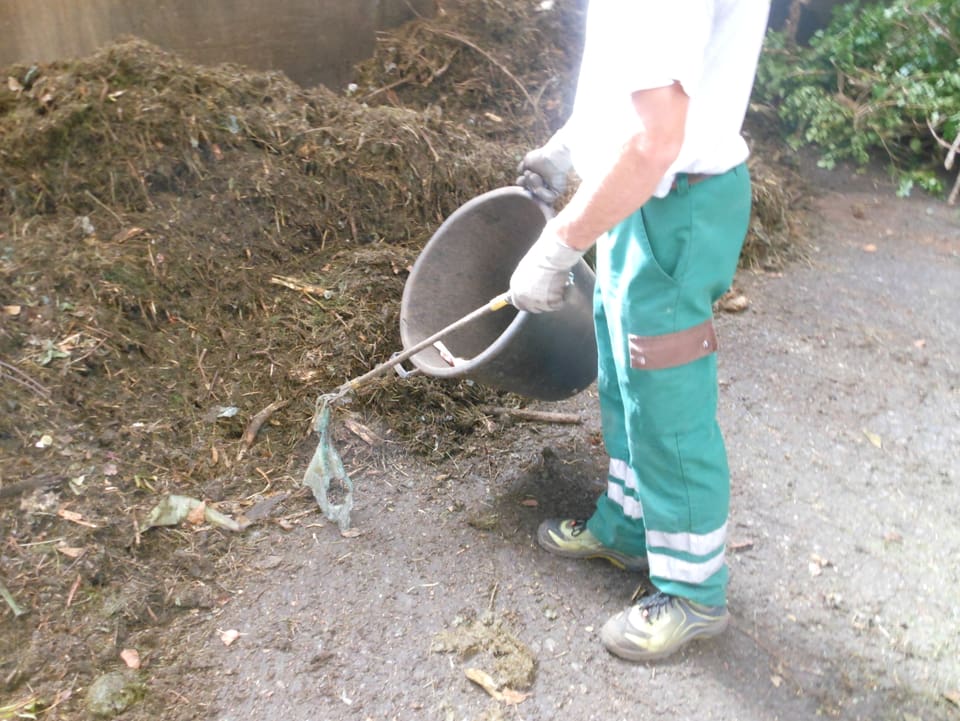 Ein Arbeiter sammelt mit einer Kneiffzange Plastikabfälle ein.