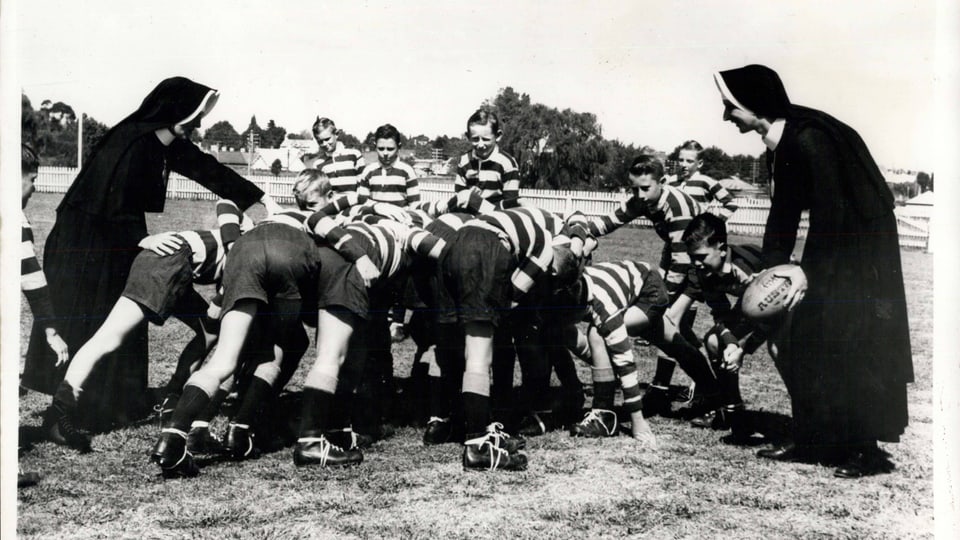 Schwarz-weiss-Bild: Eine Gruppe Buben spielt Rugby; zwei Ordensschwestern spielen mit