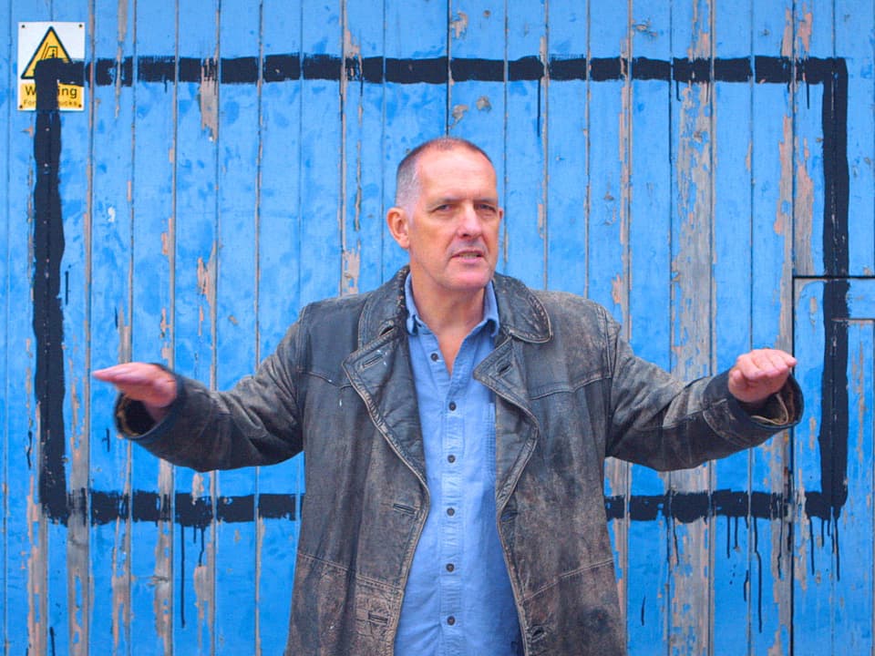 Ein Mann steht vor einer blauen Holzwand.