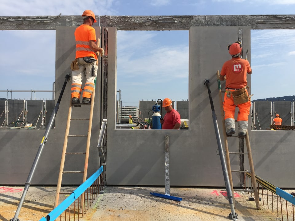 zwei Bauarbeiter in orangen Leuchtwesten stehen auf Leitern