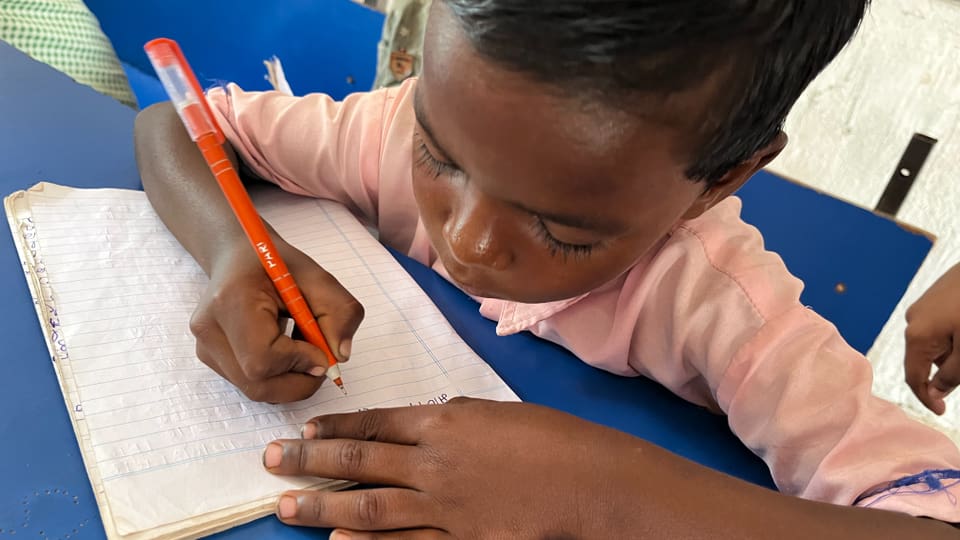 Ein Kind schreibt mit einem orangefarbenen Stift in ein Schulheft.