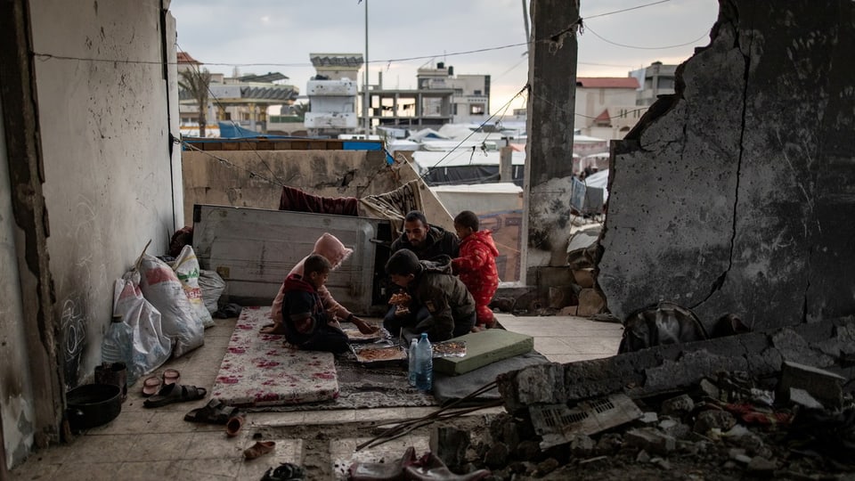 Eine Familie in Gaza-Stadt beim Essen. Sie sitzt in einem zerstörten Haus auf dem Boden.