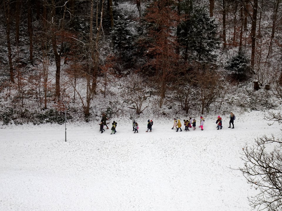 Spielende Kinder am Waldrand im Schnee.