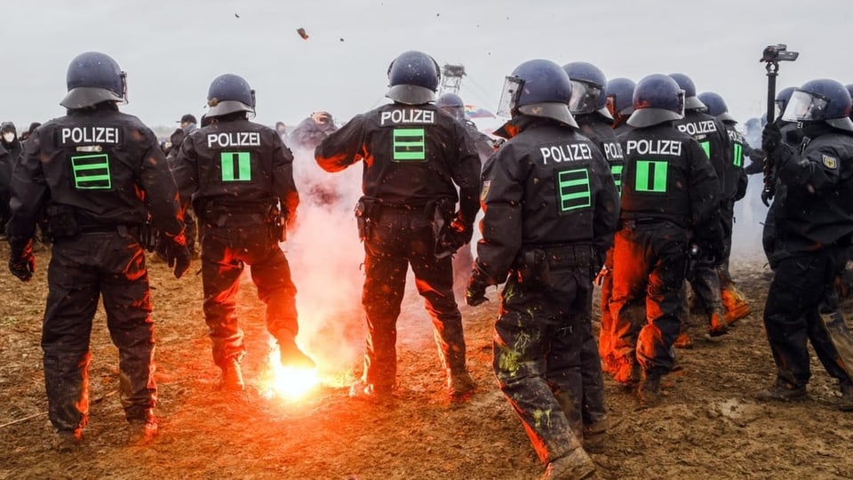 Polizisten in schwarzer Uniform und Helm, am Boden glüht ein Brandkörper