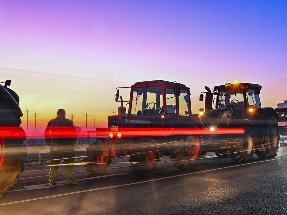 Long exposure photo: Tractor lights appear as red streaks at dawn.