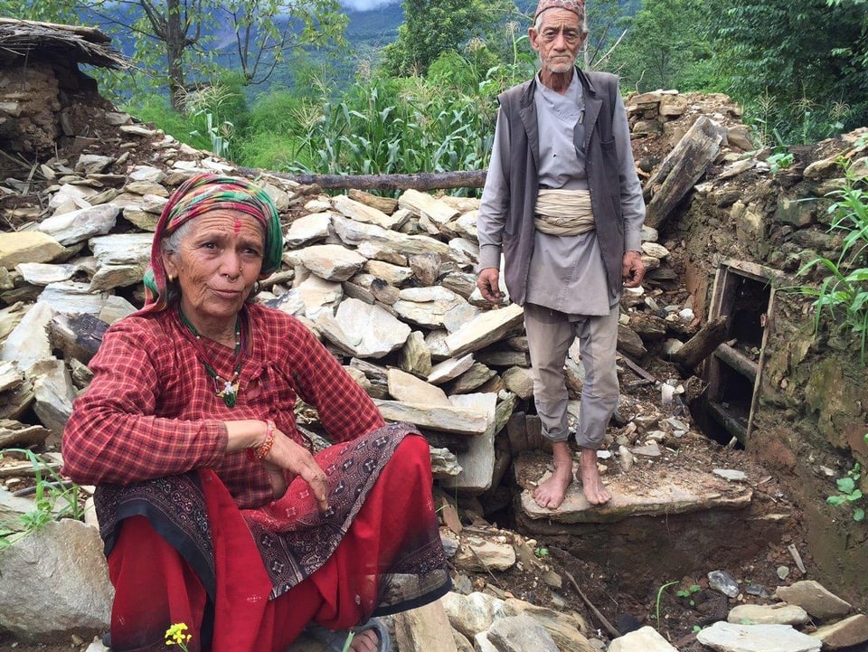 Ein älterer Mann und eine ältere Frau vor den Trümmern ihres Hauses