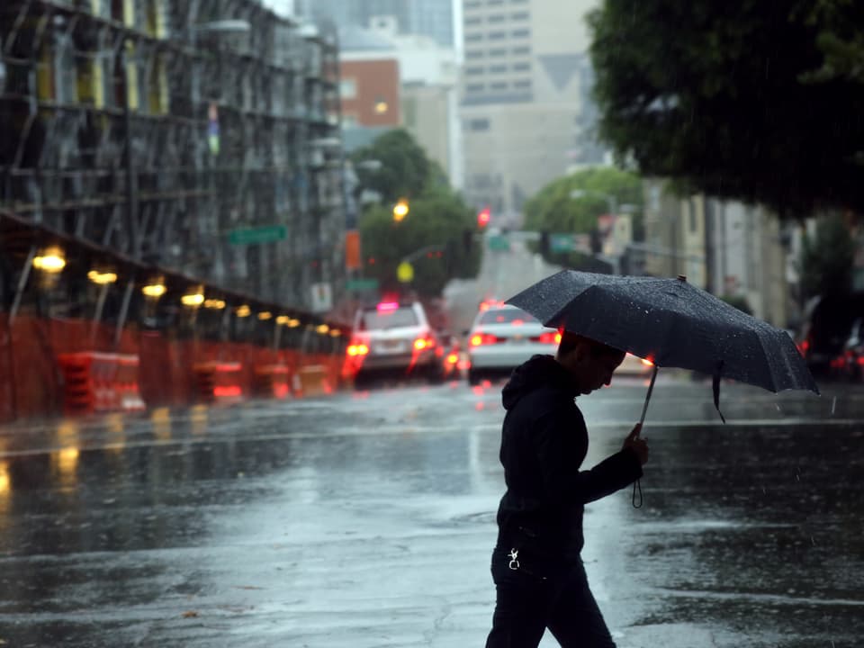 Ein Mann mit einem Regenschirm überquert eine Strasse.