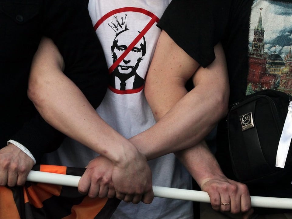 Personen halten ein Transparent und eine Person trägt ein Anti-Putin-T-Shirt.