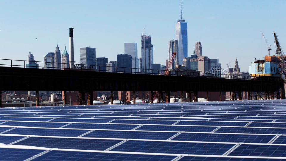 Symbolbild: Fotovoltaikanlage im Vordergrund, im Hintergrund die Skyline von New York City.