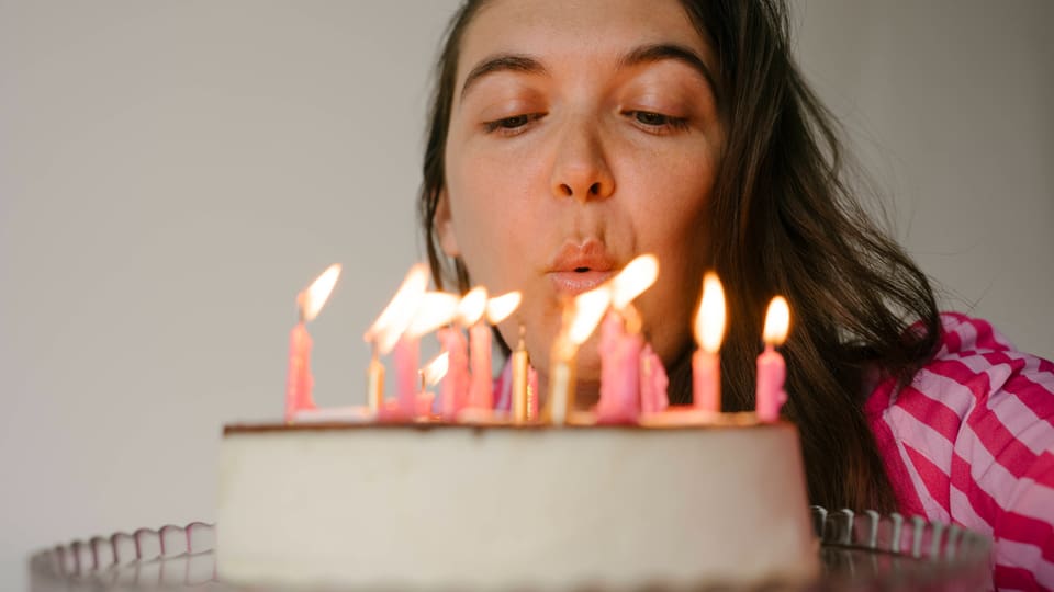 Symbolfoto: Junge Frau bläst Kerzen auf Geburtstatstorte aus