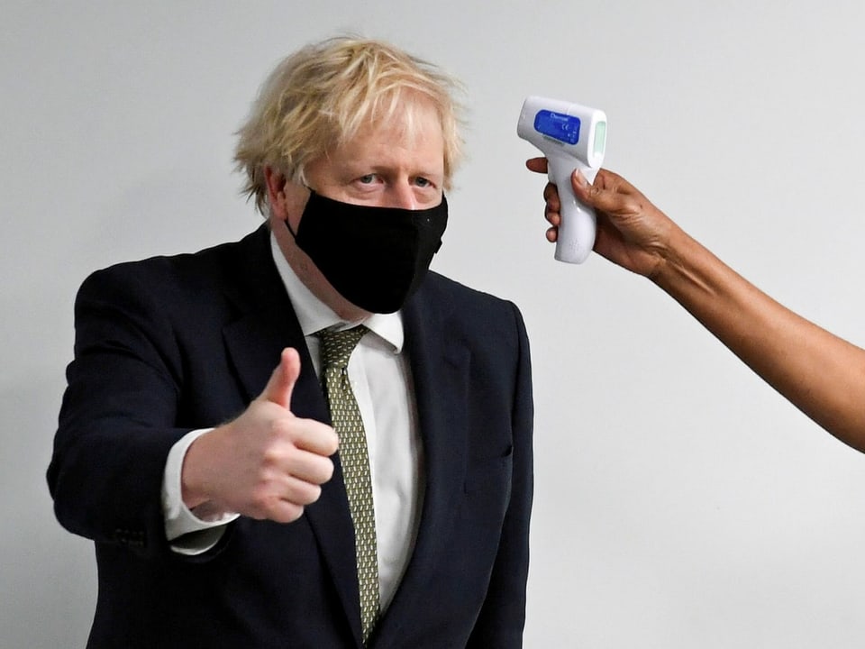 Johnson trägt eine Maske, bei ihm wird an der Stirn Fieber gemessen.