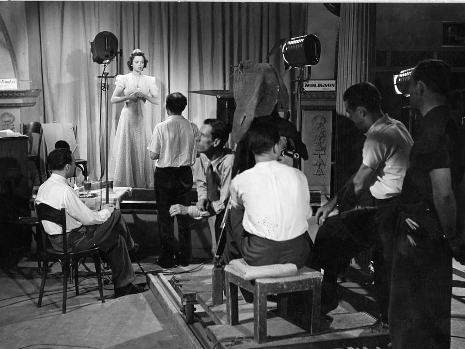 Eine Frau im Abendkleid (Jeanette) steht auf einer Bühne und wird von drei Filmscheinwerfern beleuchtet. Im Vordergrund befinden sich Crewmitglieder sowie die Kamera.