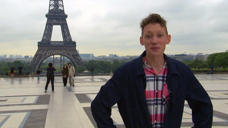 Von der Bretagne bis auf die Insel La Réunion: Moderator Jonas Modin steht auf einem Platz. Im Hintergrund sieht man den Eiffelturm