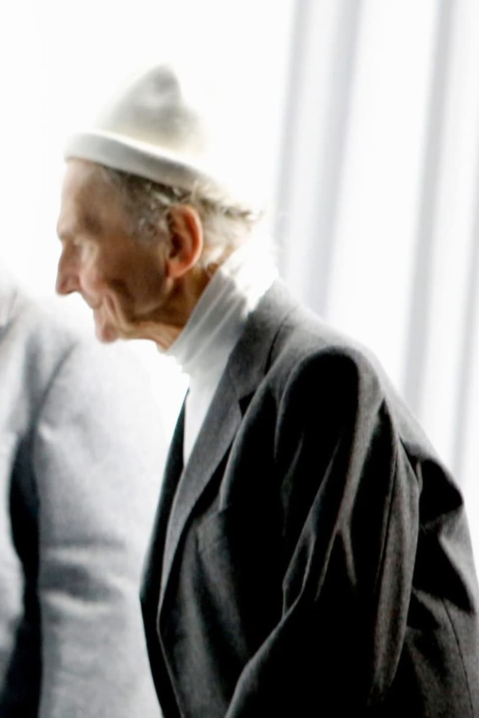 Alter Mann in Sakko, weissem Rollkragenpullover und mit weisser Mütze