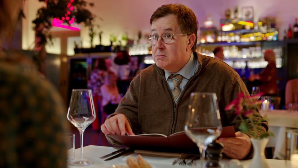 Mann sitzt mit Speisekarte im Restaurant und blickt erstaunt.