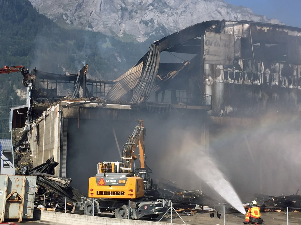 Eine zerstörte Industriehalle nach einem Grossbrand. Die Feuerwehr muss noch einzelne Glutnester bekämpfen. 