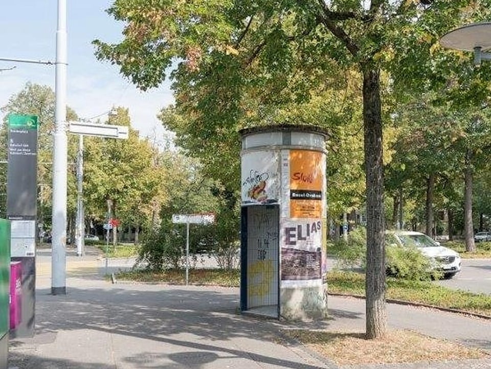 Eine Telefonkabine steht unter einem Baum auf einem grossen Platz.