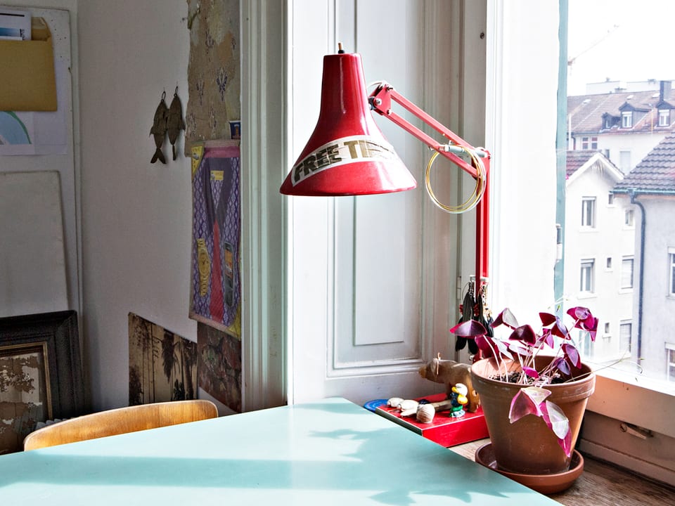 Tisch und rote Tischlampe, die auf dem Fenstersims einer Altbauwohnung steht.