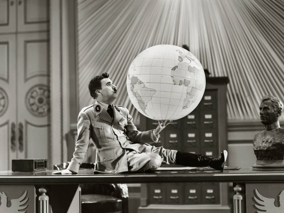 Mann mit Uniform sitzt auf einem Schreibtisch und hält eine Weltkugel in der Hand.