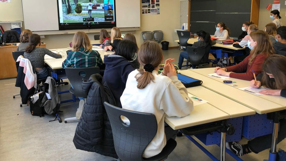 Schülerinnen und Schüler blicken in einem Klassenzimmer auf eine Leinwand