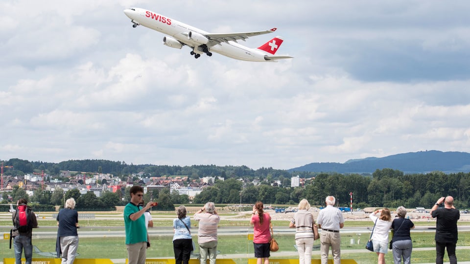 Menschen an der Landebahn beobachten ein Swiss-Flugzeug beim Abheben.