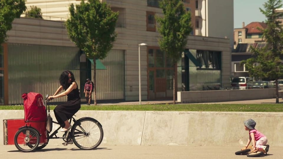Eine Mutter sitzt auf dem Fahrrad und blickt zurück auf ihr Kind, das auf dem Boden liegt.