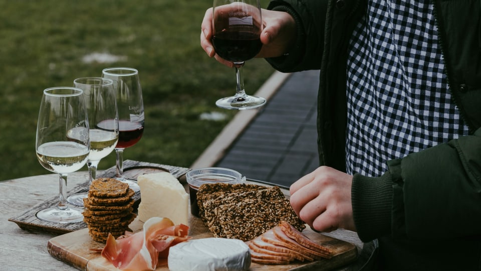 Käseplatte und Weingläser gefüllt mit Rot- und Weisswein. Ein Mann hält ein Glas Rotwein in der Hand.