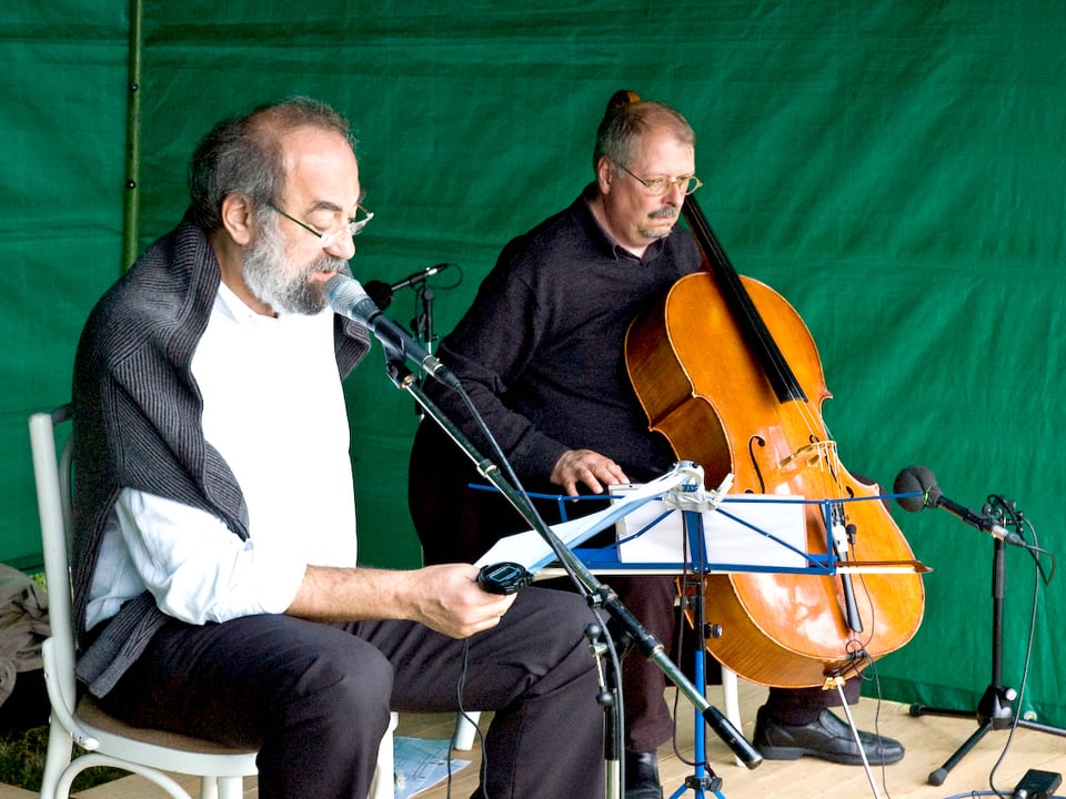 zwei Männer im Zelt, einer liest, der andere musiziert.