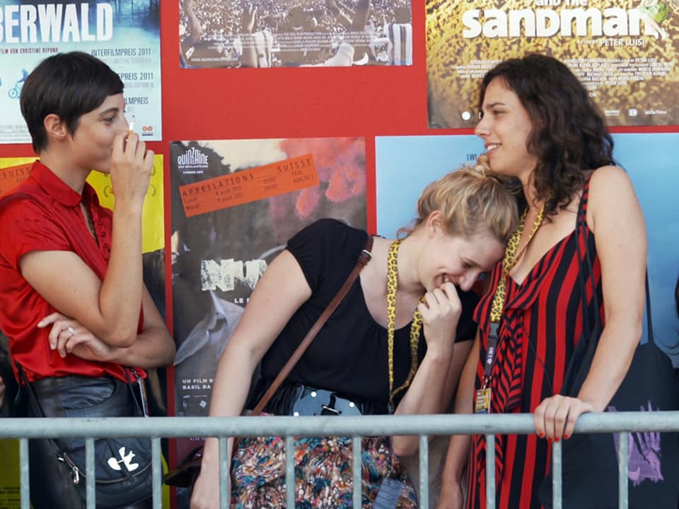 Drei Frauen stehen lachend vor Filmplakaten.