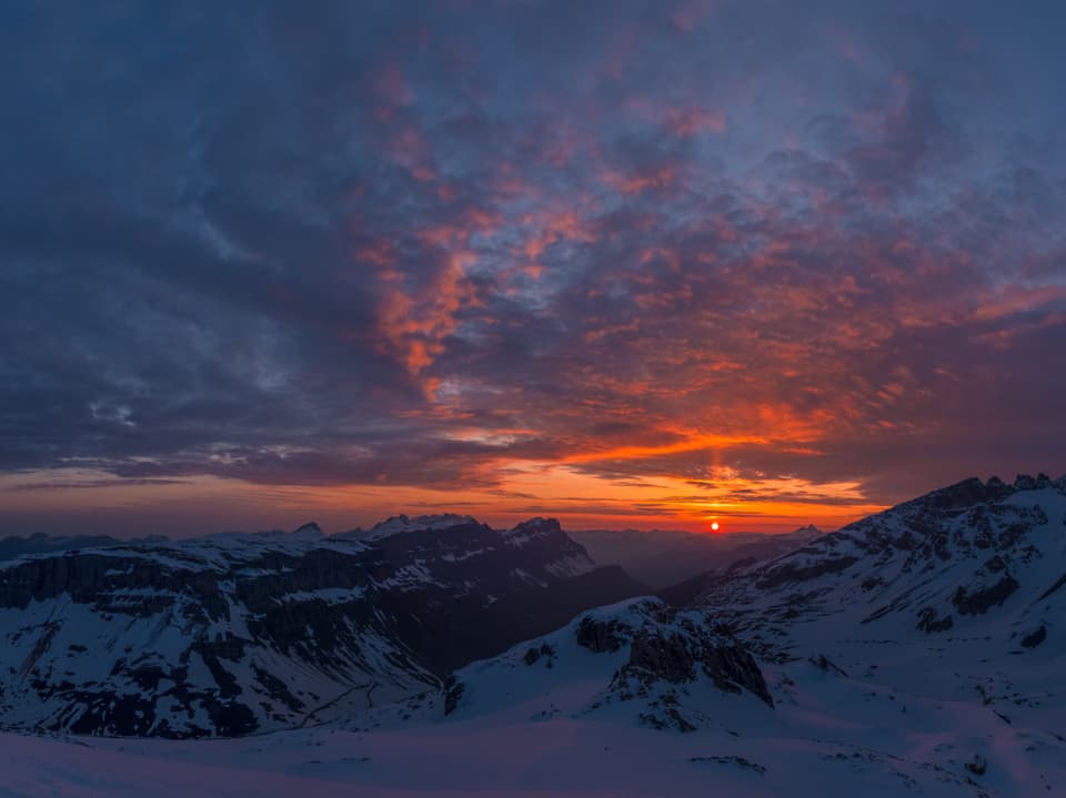 Sonnenaufgang in den Schneebergen mit Wolken am Himmel und orangem und gelbem Horizont.