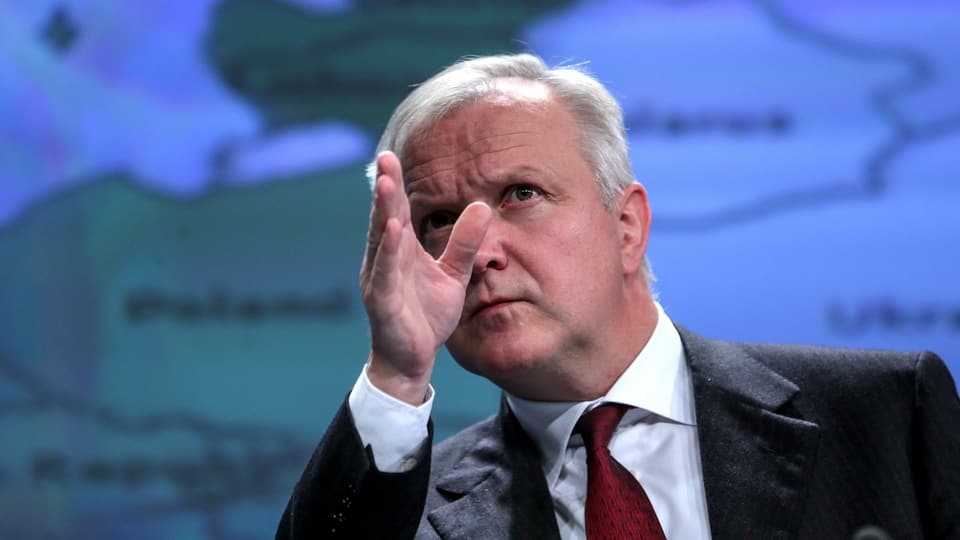 Olli Rehn vor einer Europa-Karte. Er zeigt mit der Hand nach oben.